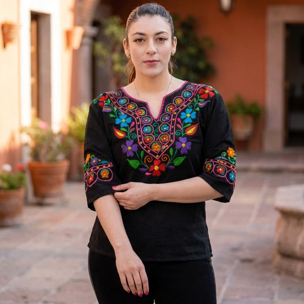 Woman wearing the black embroidered Mexican blouse in a sunny courtyard