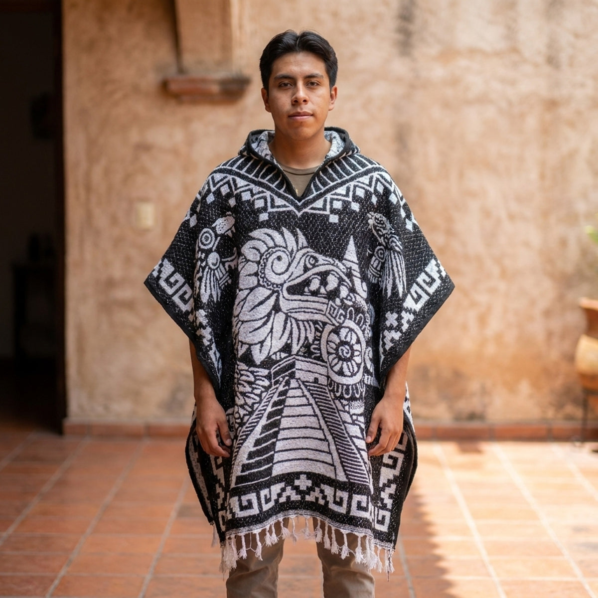 Black and white Aztec gabán poncho with Quetzalcóatl and a pyramid by a hacienda wall